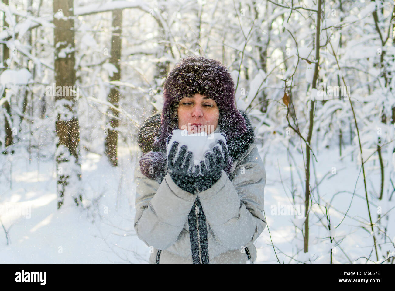 Hält eine Frau eine Handvoll Schnee in den Händen und bläst. Winter im Wald. Die sonne funkelt. Tag, Russland. Stockfoto