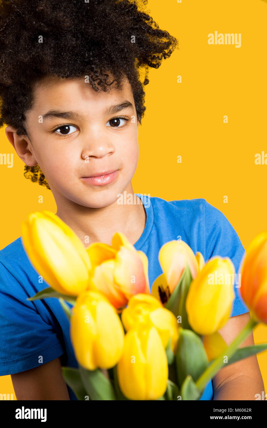 Adorable kleinen Jungen mit einem blauen T-Shirt mit einem Tulpen Bouquet. Auf gelb isoliert Stockfoto