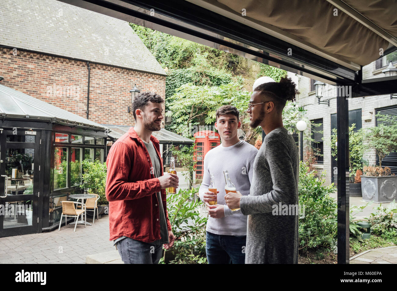 Drei Männer stehen im Hof eines Bar. Sie erfreuen sich im Gespräch beim Bier trinken. Stockfoto