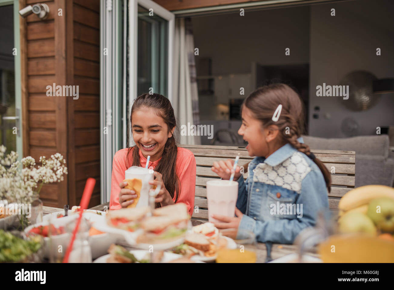 Zwei kleine Mädchen genießen Milchshakes außerhalb Ferienhaus. Stockfoto