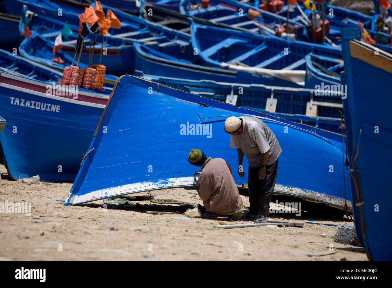 Fischer malen ihre blauen Boote aus Holz in der Stadt Plage d'Imsouane in der Nähe von Essaouira, Marokko. Stockfoto