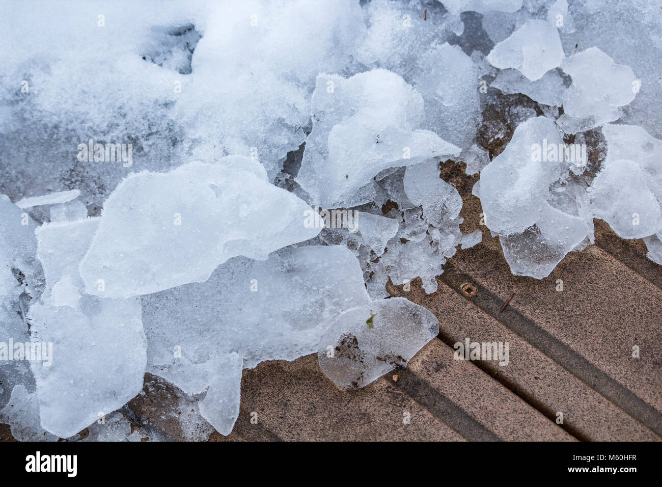 Ein semi-abstrakte Sicht der kontrastierenden Farben und Texturen der eisigen Brocken der Schnee neben einem gelöscht Teil eines hölzernen Deck. Stockfoto