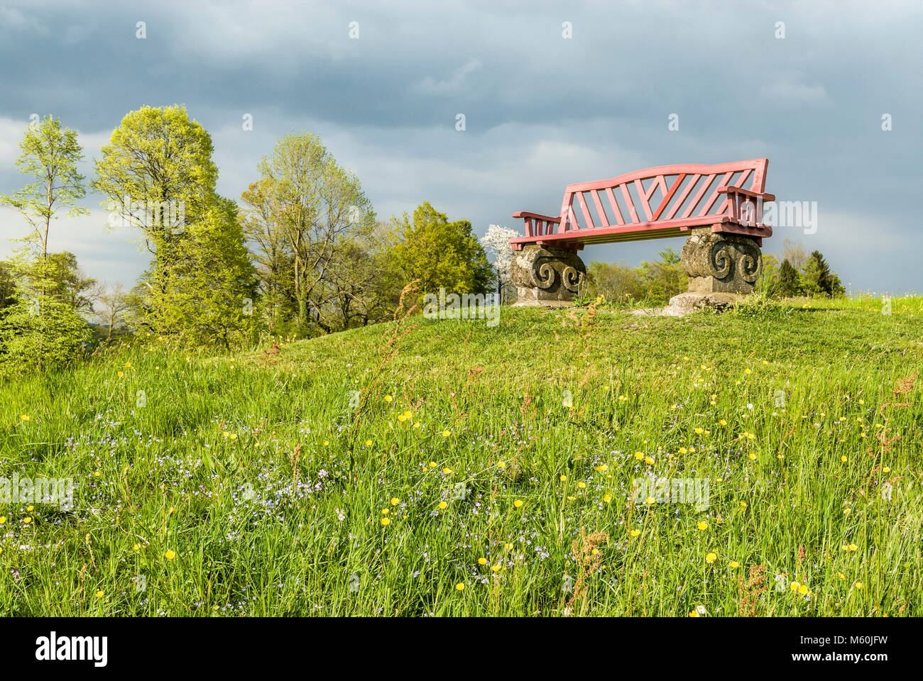 Einsame und leere Bank auf einem grünen Spring Lawn Hill mit Blumen, Schweiz Stockfoto