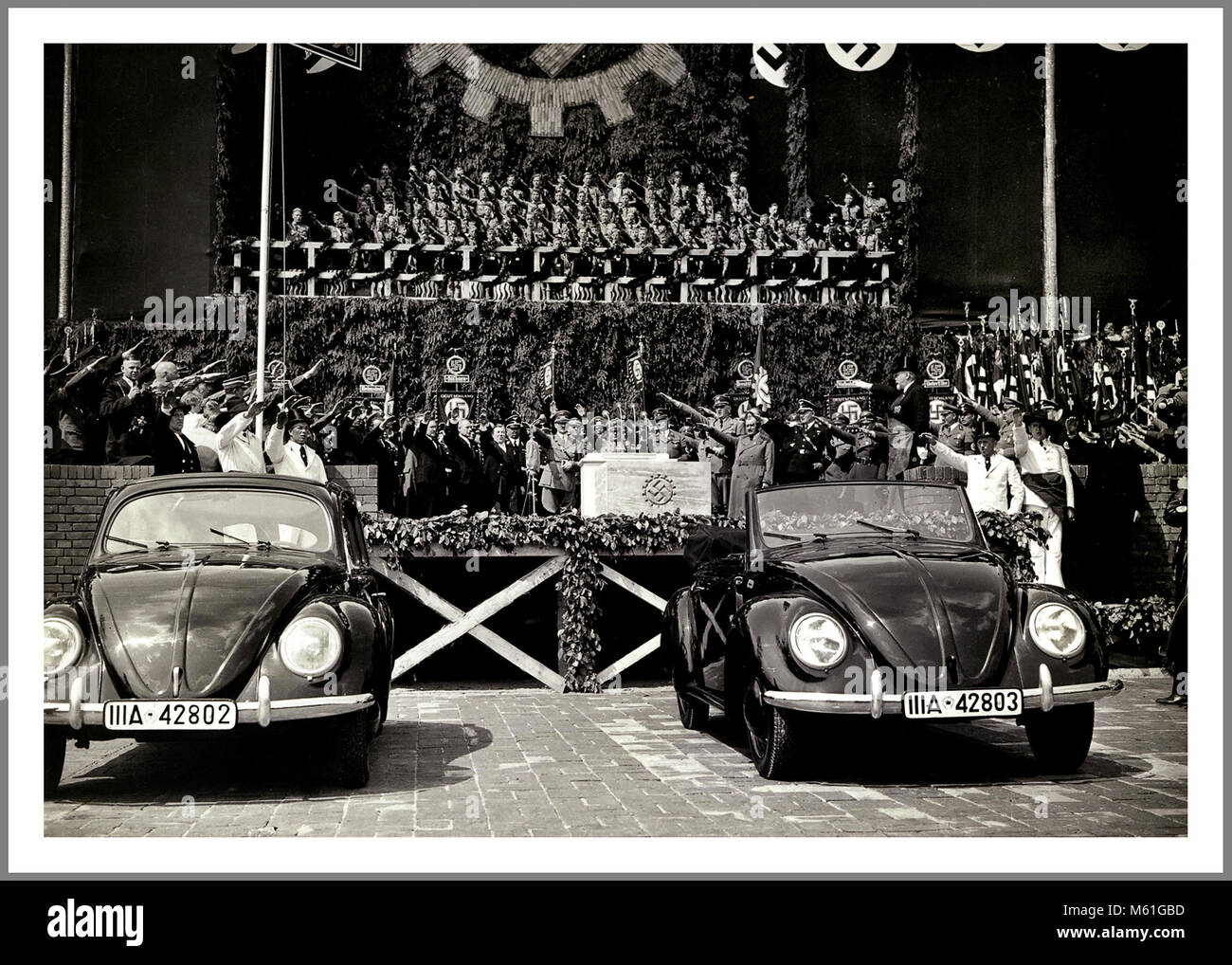 VOLKSWAGEN KdF-Wagen Start mit Adolf Hitler Nazi Deutschland Propagandabild 26. Mai 1938 Hakenkreuz Emblem Grundsteinlegung mit Adolf Hitler und Dr. Porsche und Beamte grüßen Heil Hitler im Volkswagen Werk Fallersleben Wolfsburg mit der bahnbrechenden neuen KdF - Wagen (Kraft durch Freude) Volkswagen Limousine und Cabriolet unter Nazi Hakenkreuz Fahnen Stockfoto