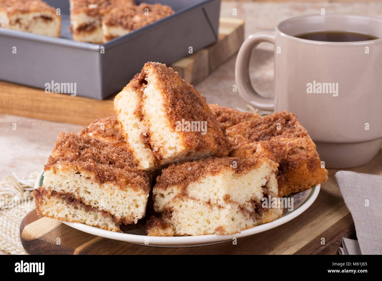 In Scheiben geschnitten Zimt swirl Kaffee Kuchen auf eine Platte mit Tasse Kaffee und Backblech im Hintergrund Stockfoto