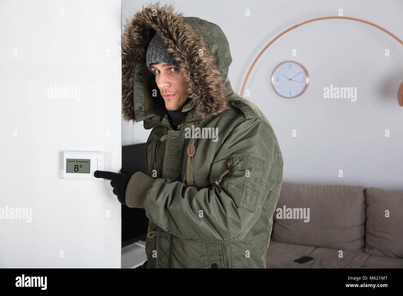 Junger Mann in warme Kleidung, die auf aktuelle Raumtemperatur in Digitaler Thermostat zu Hause Stockfoto