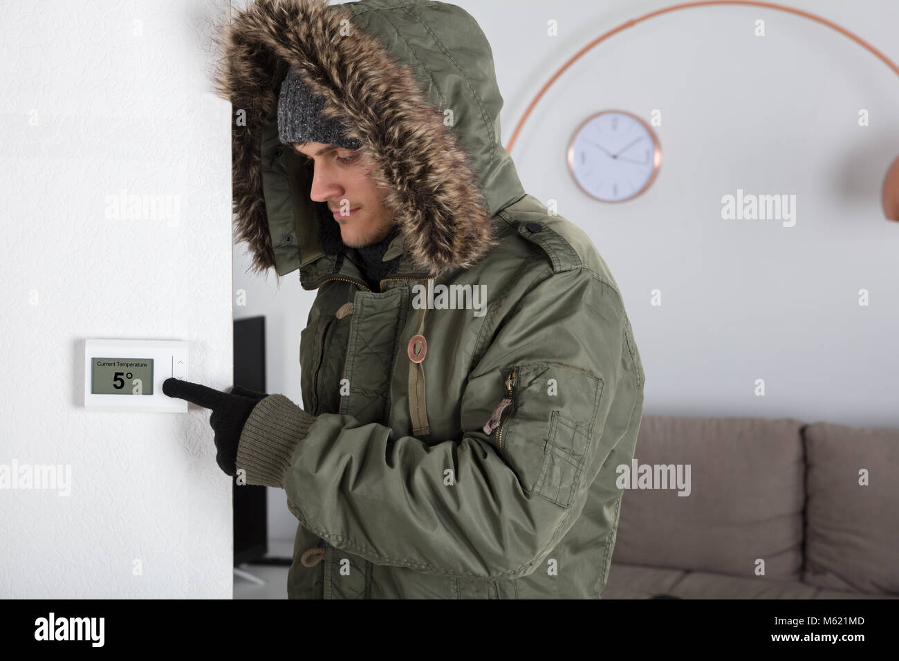 Junger Mann in warme Kleidung, die auf aktuelle Raumtemperatur in Digitaler Thermostat zu Hause Stockfoto