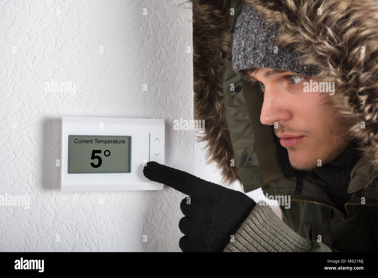 Junger Mann in warme Kleidung, die auf aktuelle Raumtemperatur in Digitaler Thermostat zu Hause Stockfoto