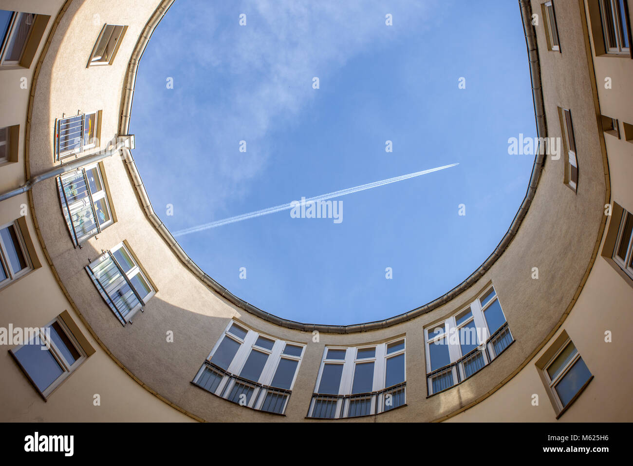 Flugzeug fliegen über die Eröffnung eines Hinterhof verlassen ein kondensstreifen. Berlin, Deutschland, Europa. Stockfoto