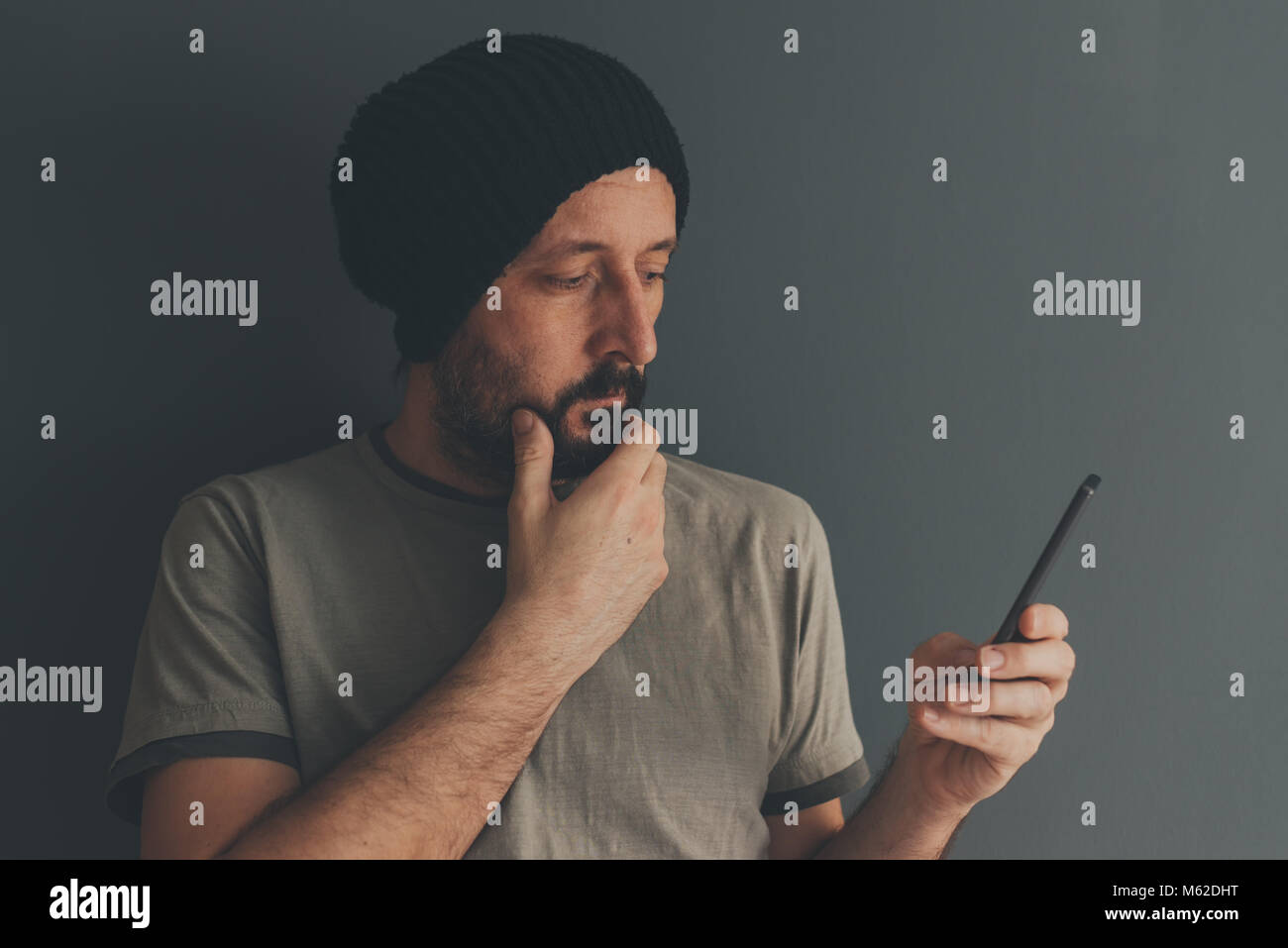 Casual erwachsenen Mann mit Kappe am Handy suchen, Low Key Kommunikation und Lifestyle Portrait mit selektiven Fokus Stockfoto