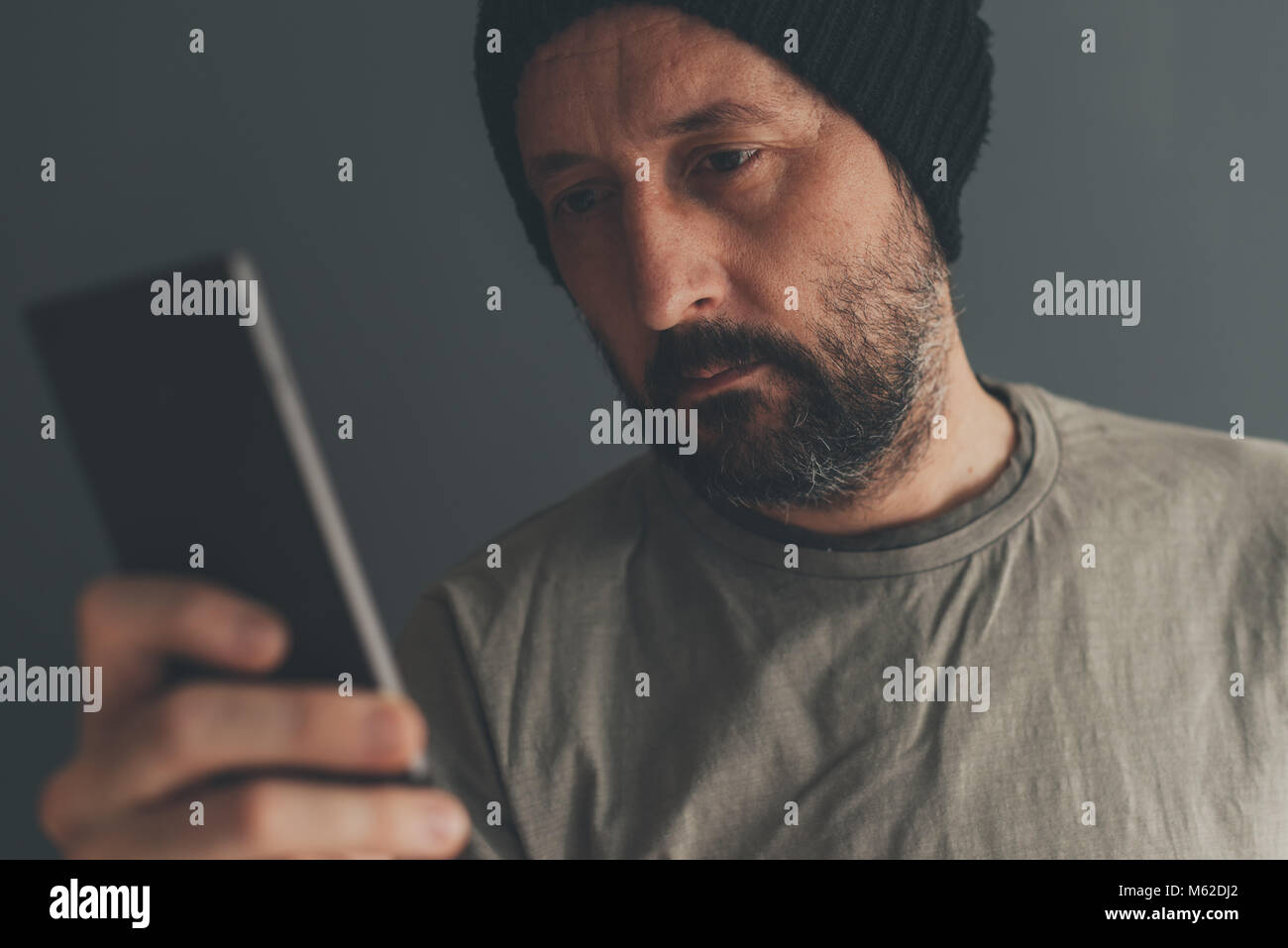Casual erwachsenen Mann mit Kappe am Handy suchen, Low Key Kommunikation und Lifestyle Portrait mit selektiven Fokus Stockfoto