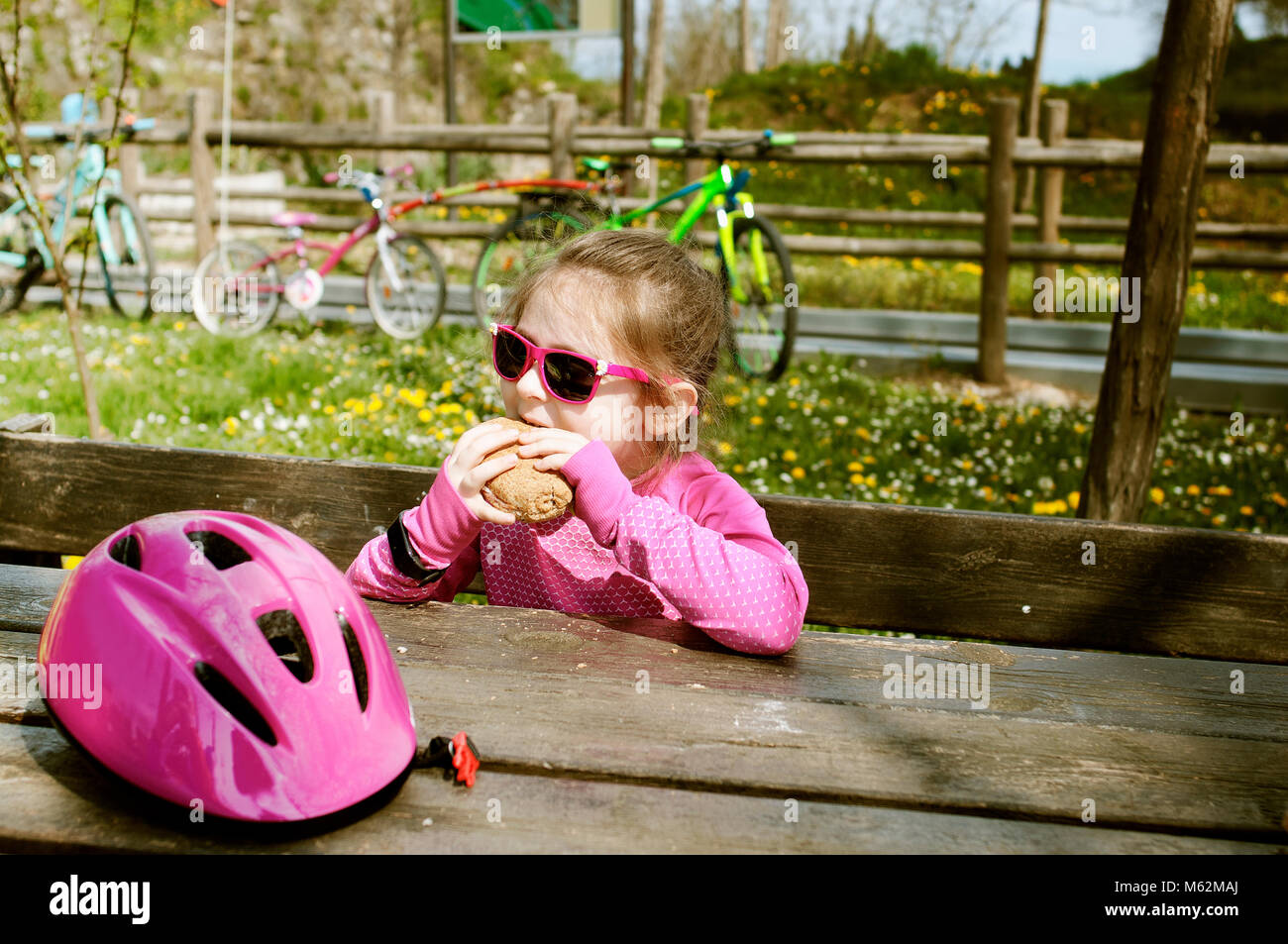 Ein kaukasischer bike Rider 6 jähriges Mädchen haben ein Mittagessen auf einer Bank im Freien. Stockfoto