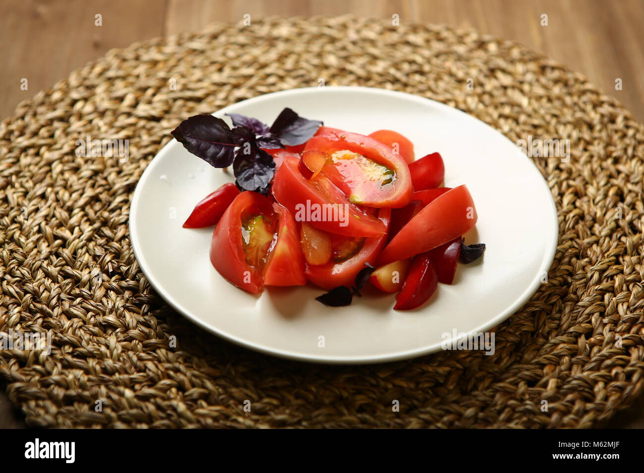 Salat von Tomaten und rote Pflaumen mit Basilikum für eine gesunde Ernährung. Kalorienarme Nahrung für Körper Gewicht kontrollieren. Schnelle Snacks. Auf einem Holztisch, ein Korb stehen. Stockfoto