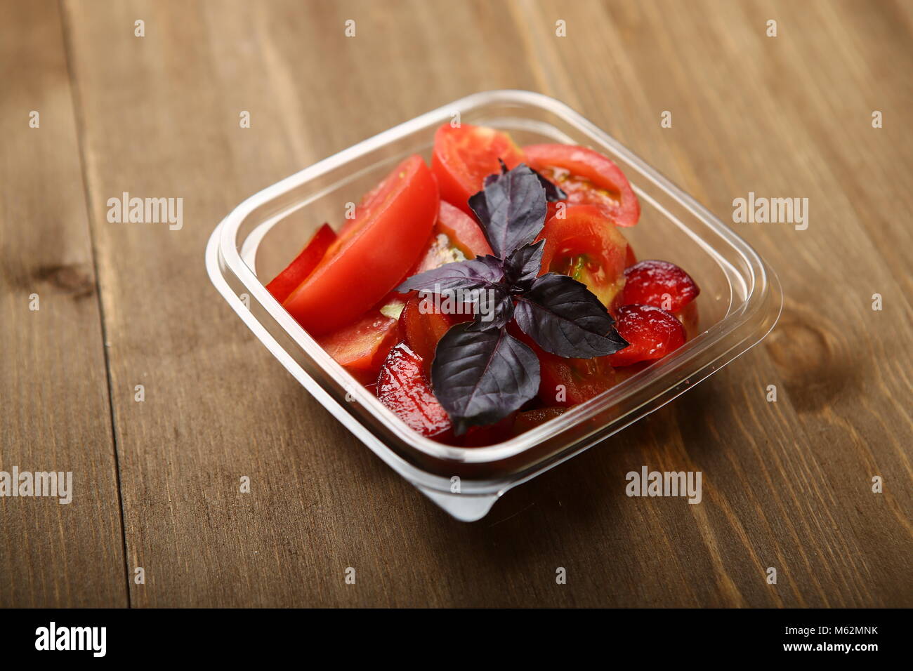 Salat von Tomaten und rote Pflaumen mit Basilikum für eine gesunde Ernährung. Lieferung nach Hause, sie in einem transparenten Plastikbehälter. Kalorienarme Lebensmittel Körper w zu steuern Stockfoto