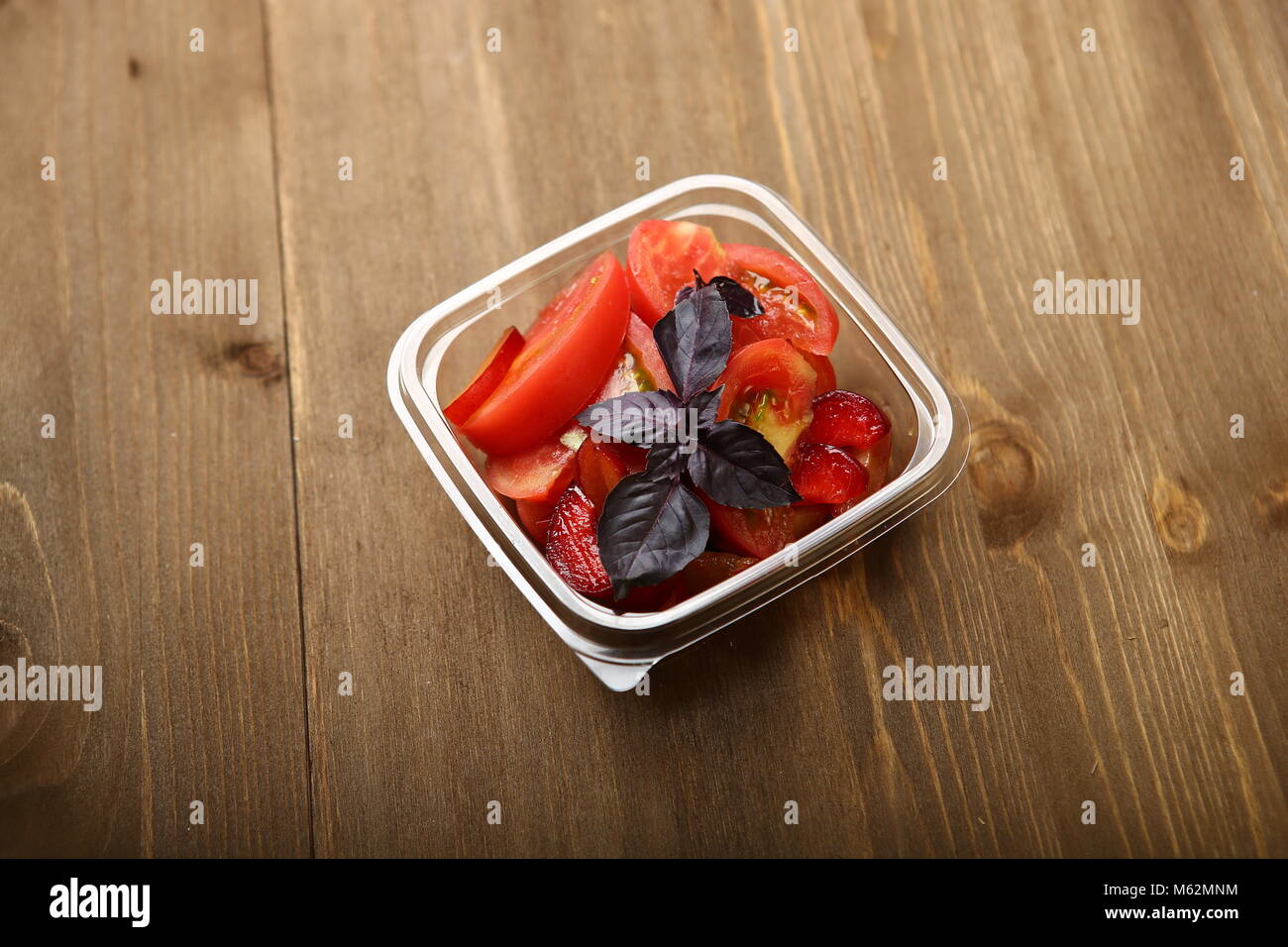 Salat von Tomaten und rote Pflaumen mit Basilikum für eine gesunde Ernährung. Lieferung nach Hause, sie in einem transparenten Plastikbehälter. Kalorienarme Lebensmittel Körper w zu steuern Stockfoto