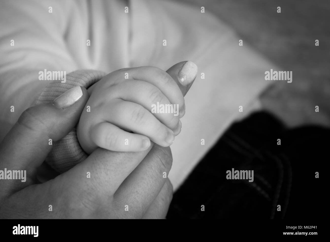 Kleines Baby Hand hält Mama's Finger mit lackierten Nägeln. Familie, Liebe, Zärtlichkeit, Vertrauen, Mutterschaft Konzepte. Die Schwarz-Weiß-Fotografie Stockfoto