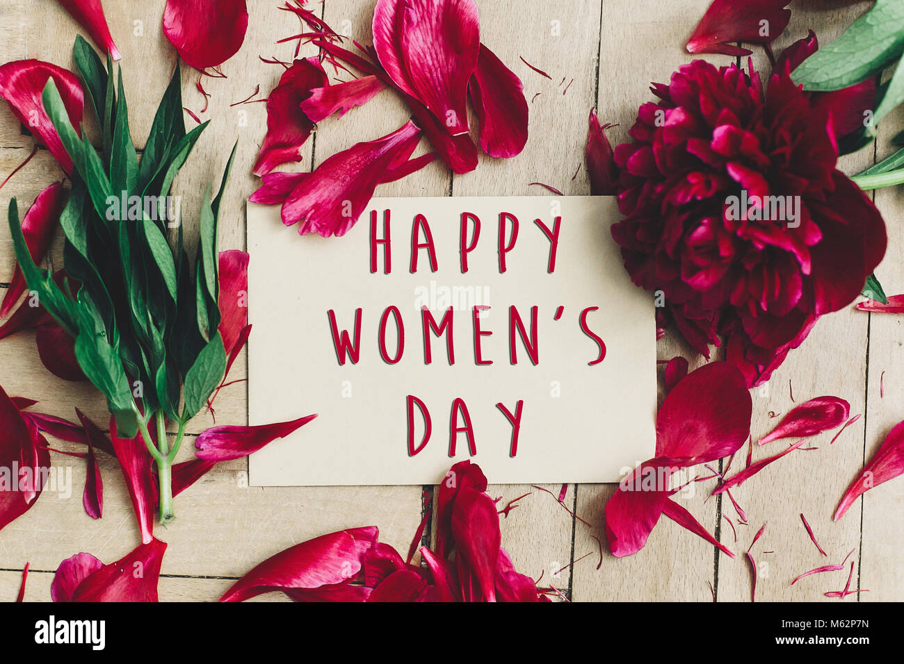 Der glückliche Frauen Tag Text Zeichen für das Handwerk Karte und schönen roten Pfingstrosen auf Holz rustikale Hintergrund, flach. Moderne Grußkarte. Tag der Frauen Stockfoto