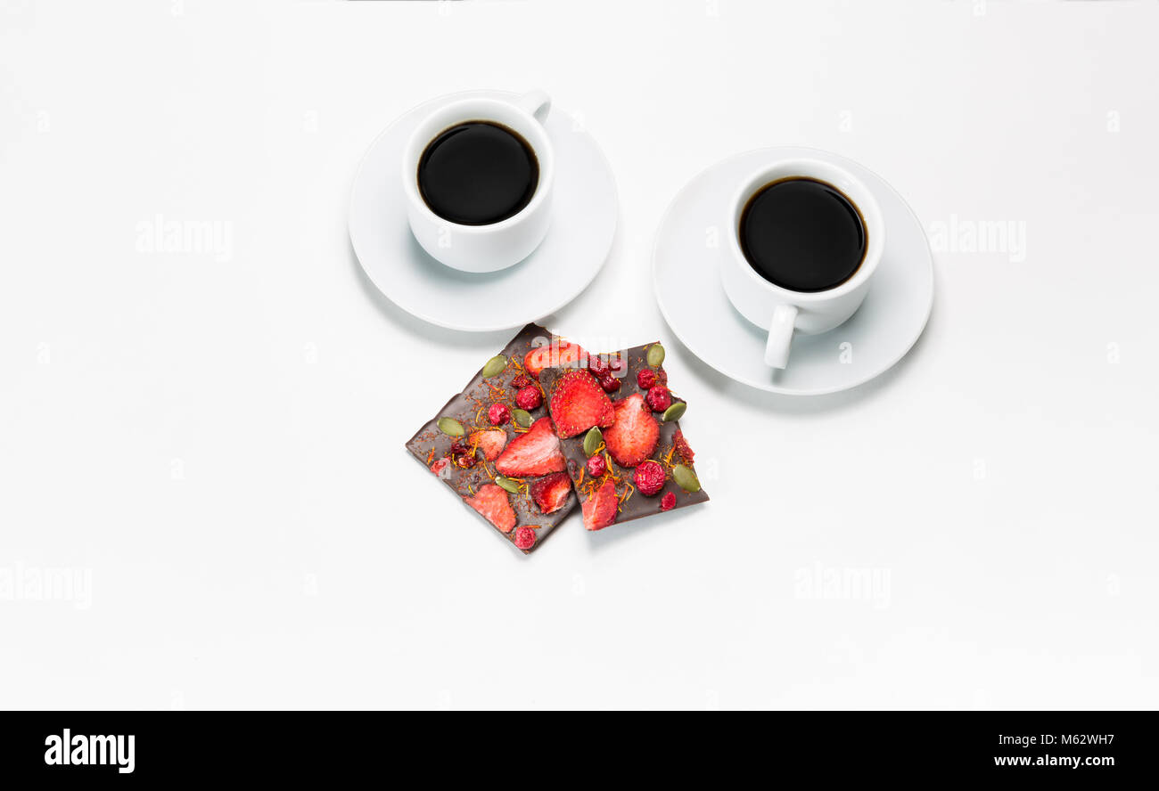 Zwei Tassen Kaffee und handgemachte Schokolade mit getrockneten Erdbeeren und Beeren auf weißem Hintergrund Stockfoto