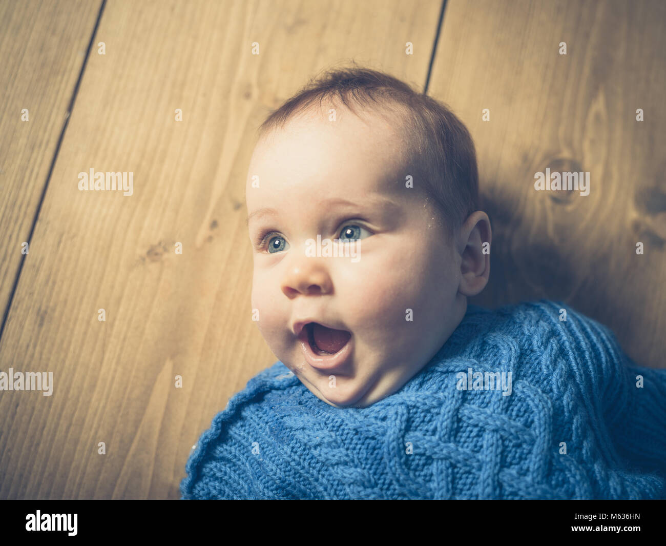 Ein glückliches und überrascht Baby liegen auf einem Holzboden Stockfoto