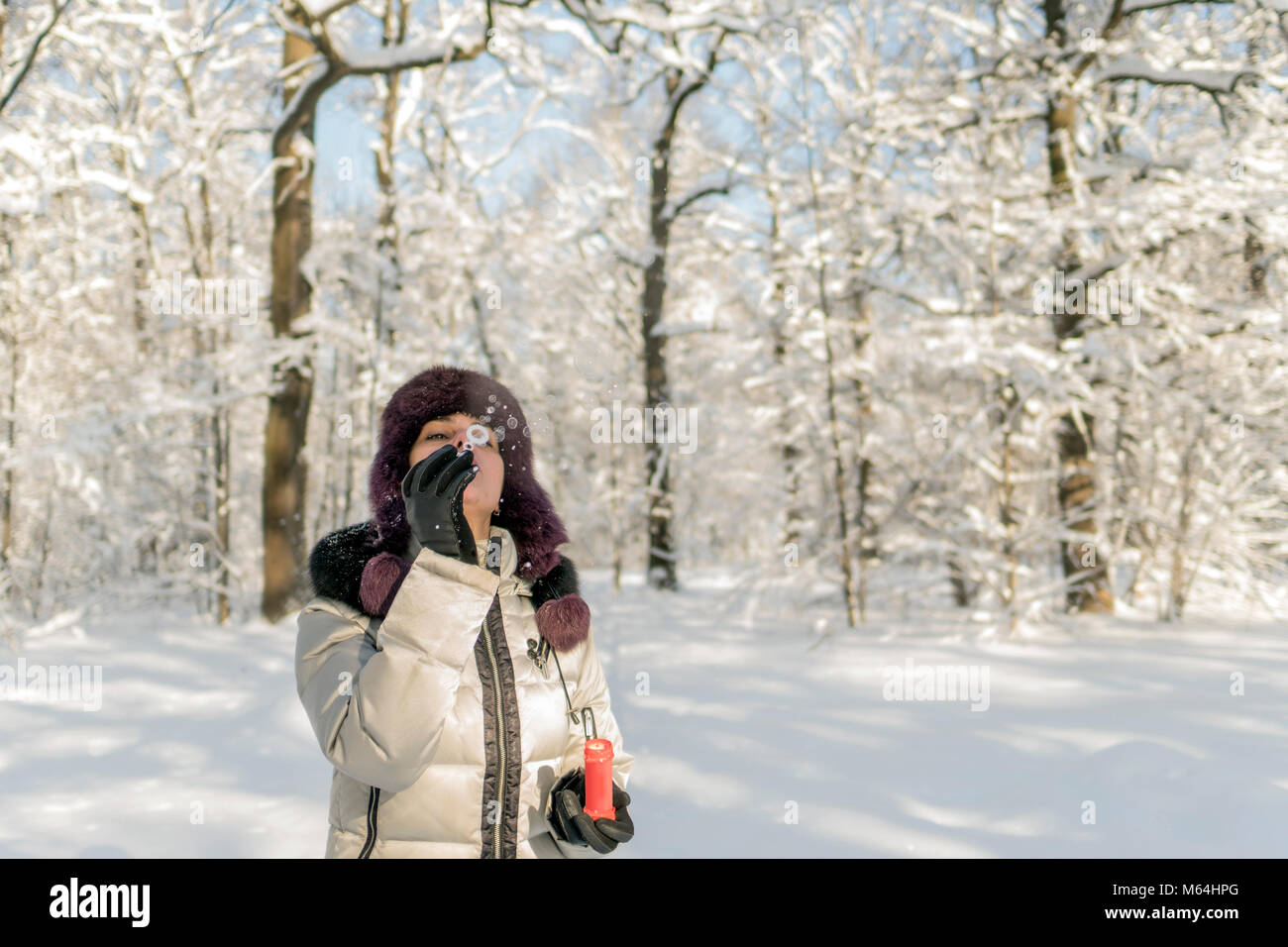 Hält eine Frau eine Handvoll Schnee in den Händen und bläst. Winter im Wald. Die sonne funkelt. Tag, Russland. Stockfoto