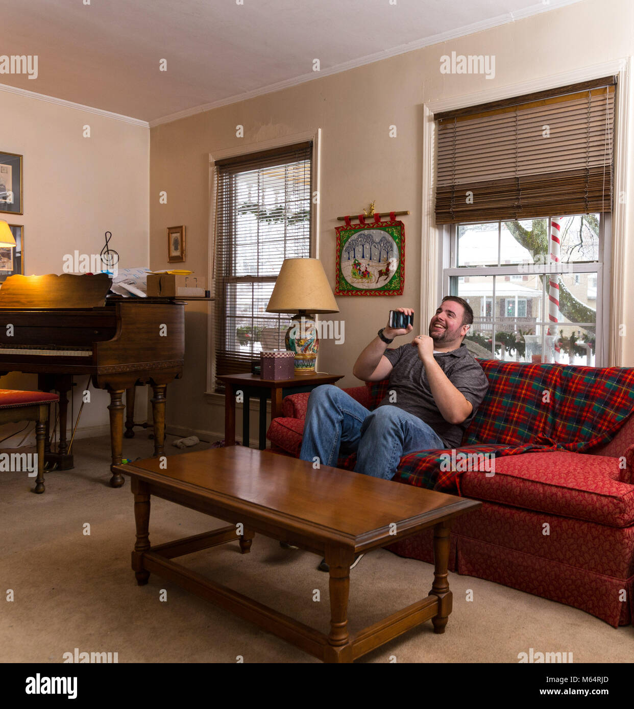 Junge kaukasier man Karaoke singen in sein Telefon beim Sitzen allein in seinem Wohnzimmer Stockfoto