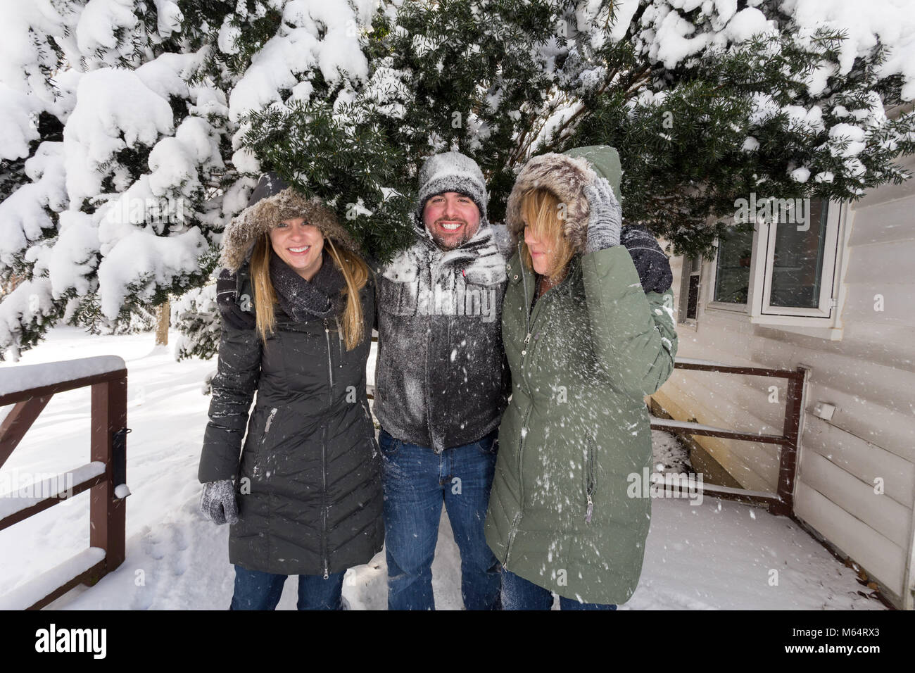 Drei junge Erwachsene Spielen im Schnee hinter einem Haus wie Sie Abdeckung und Ursache Unfug mit dem Schnee Stockfoto