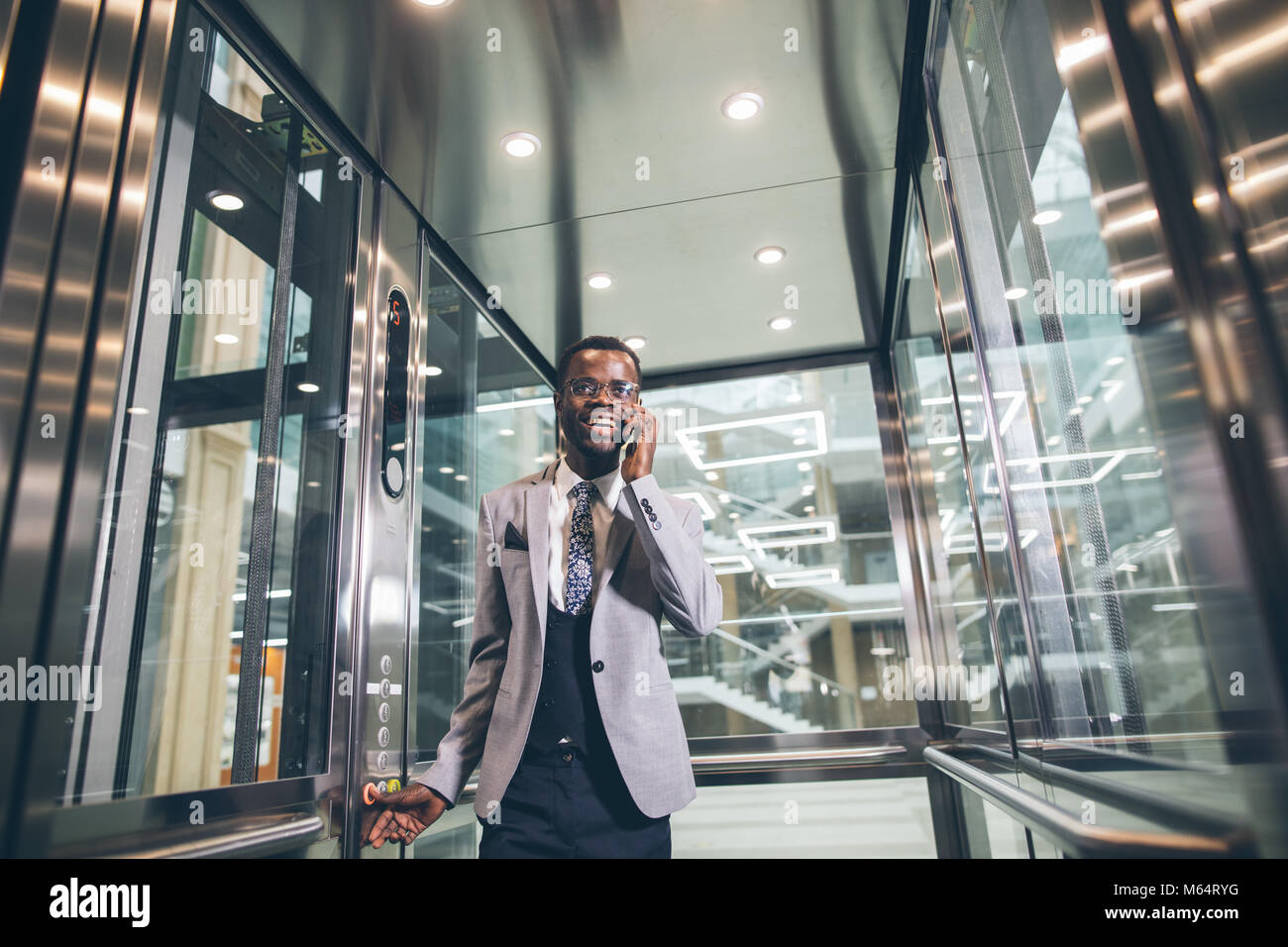 Afroamerican Geschäftsmann in der modernen Aufzug aus Glas am Telefon sprechen Stockfoto