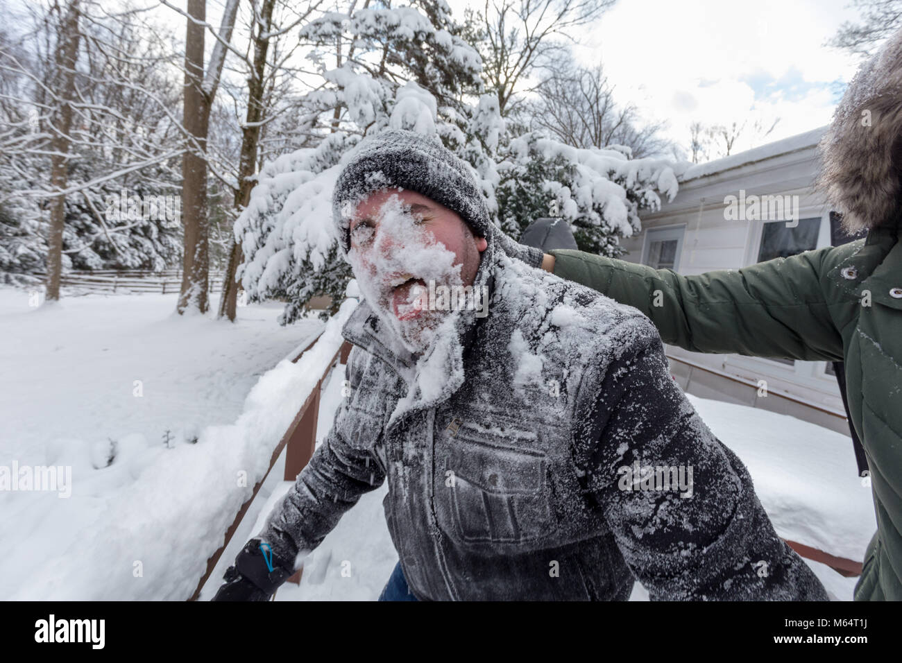 Zwei Yong Frauen im Winter Mäntel spielerisch zu drücken, um eine junge bemannt Gesicht in den Schnee Stockfoto