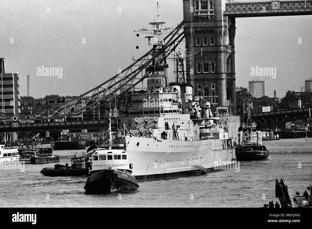 Mit Schleppern in Anwesenheit der Kreuzer HMS Belfast auf ihre Ankunft im Pool von London. Die Schlepper schleppte sie von Tilbury zurück zu Ihrer Anlegestelle in der Nähe der Tower Bridge, nach größeren Arbeit ihrem Rumpf zu bewahren. Stockfoto