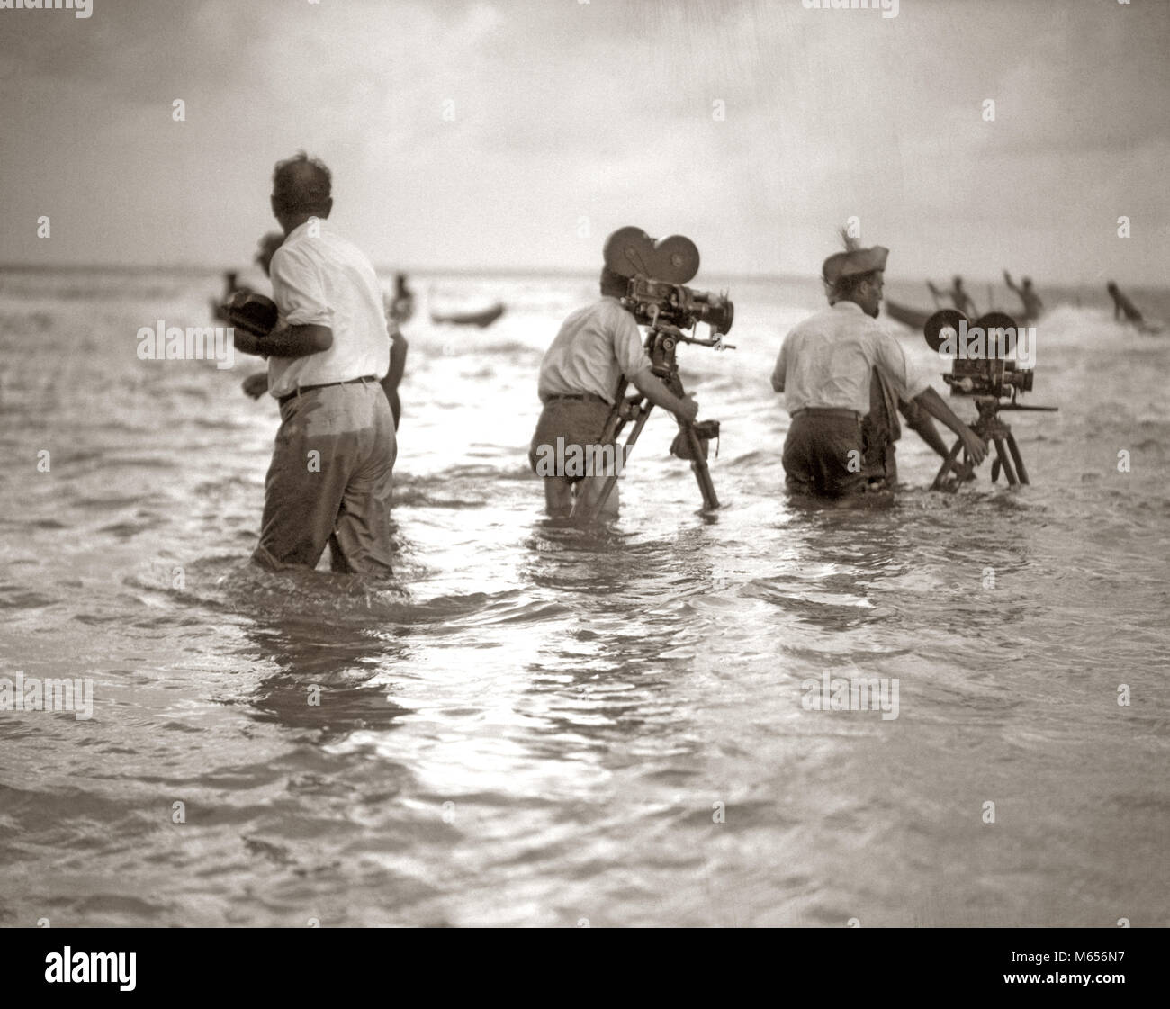 1920 Filmemacher in knietiefem Wasser Meer Dreharbeiten Dreharbeiten Kameras - f 1095 HAR 001 HARS FELSIGE ABENTEUER KARRIERE AUFREGUNG NIEDRIGEN WINKEL KOOPERATION KREATIVITÄT SCHAUSPIELER KAMERALEUTE GRUPPE VON MENSCHEN STUMMFILM MOTION PICTURE WERBUNG NOCH MÄNNER FILM NOCH IMMER SEASCAPE B&W SCHWARZ UND WEISS KAUKASISCHEN ETHNIE KAMERAMANN KAMERALEUTE filmschaffende Berufe ALTMODISCHE OUTRIGGER KANU PERSONEN Stockfoto