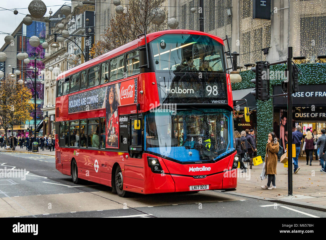 Eine Frau wartet darauf, an einer Fußgängerüberführung zu überqueren, während ein London Bus der Linie 98 nach Holborn den Weg entlang der Oxford Street in London, Großbritannien, einhält Stockfoto