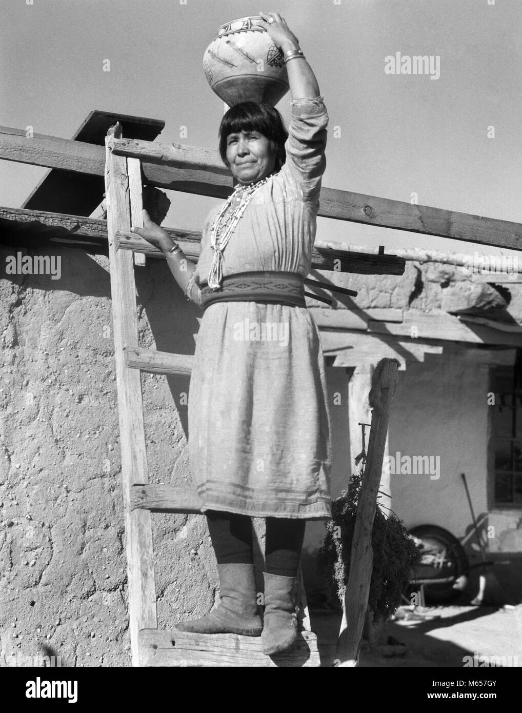 1930er Jahre native american Indian FRAU AUF LEITER HOLDING OLLA KERAMIK KRUG AUF DEM KOPF COCHITI PUEBLOS NEW MEXICO USA-i 1483 HAR 001 HARS NORDAMERIKA JAR 25-30 Jahre 30-35 JAHRE NORDAMERIKANISCHEN STÄRKE LOW ANGLE STOLZ NATIVE AMERICAN PUEBLO COCHITI MITTE NACH MITTE DER ERWACHSENEN FRAU NEW YORK B&W SCHWARZ UND WEISS EINHEIMISCHE BERUFE ALTMODISCHE OLLA PERSONEN POTTER Stockfoto