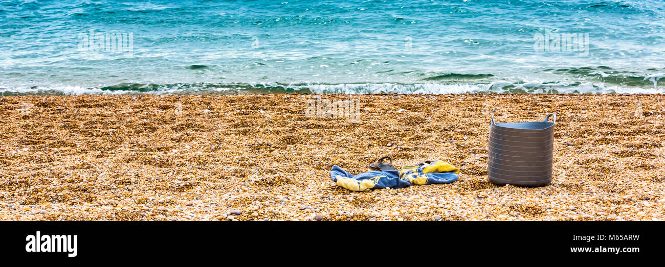 Eine Schaufel, ein Handtuch und Badeschuhe allein am Strand links beim Schwimmen. Stockfoto
