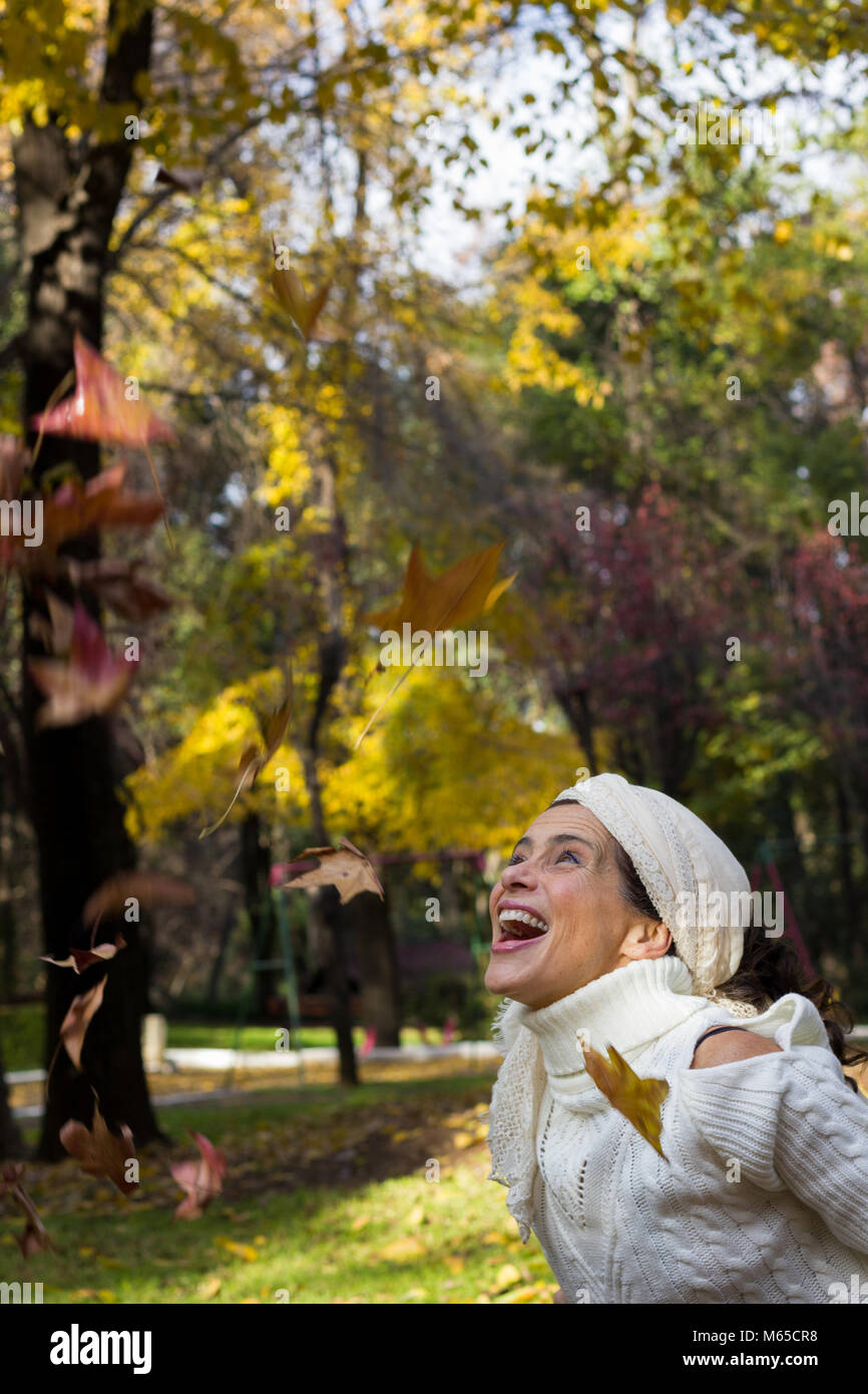 Frau mittleren Alters in Ehrfurcht an der braunen Blätter suchen in der Luft im Park im Herbst Saison überglücklich. Jubelnde, euphorische Konzept. Herbst Anreise Stockfoto