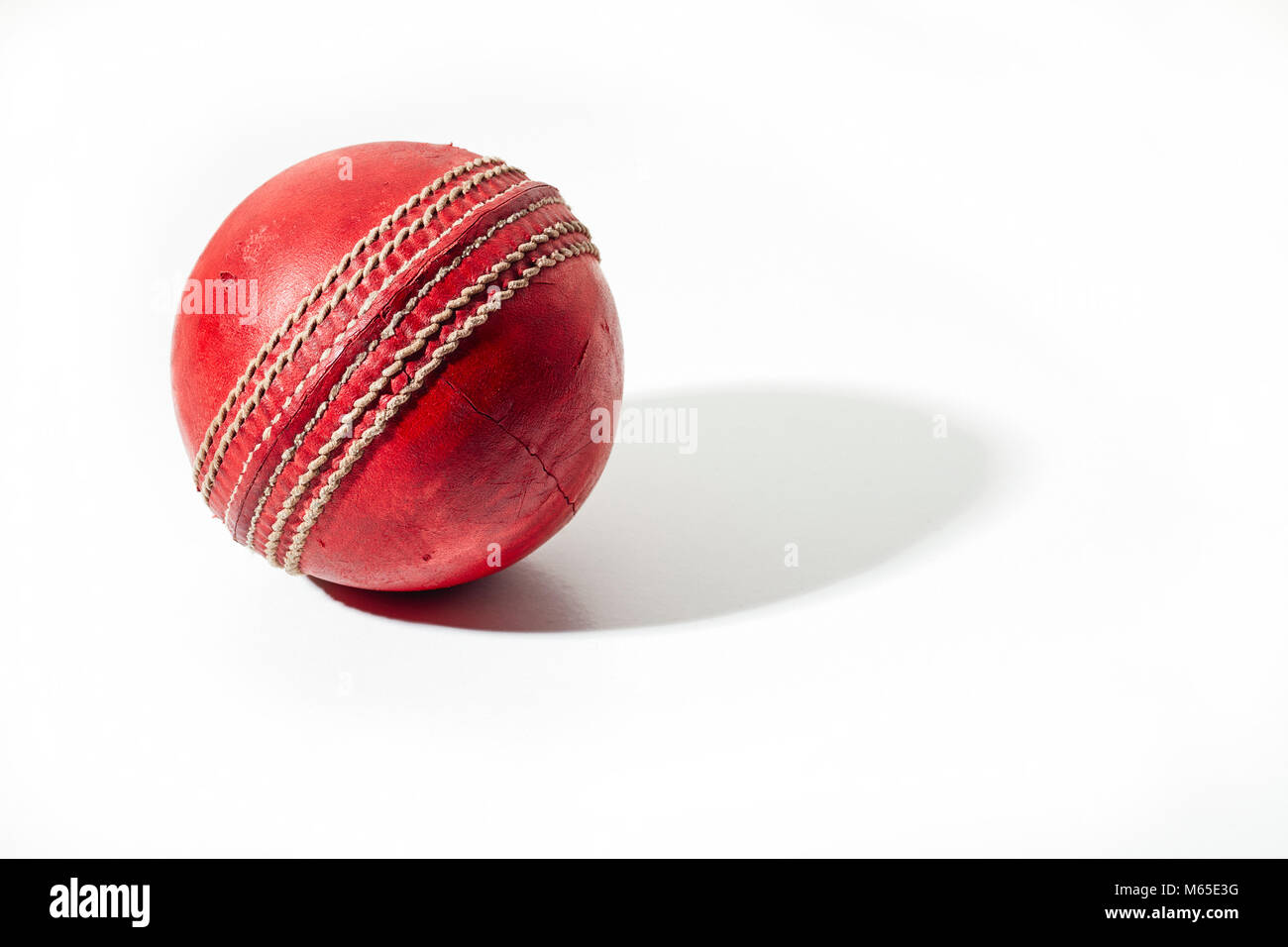 Red cricket Ball auf einem weißen Hintergrund in starke seitliche Beleuchtung Stockfoto