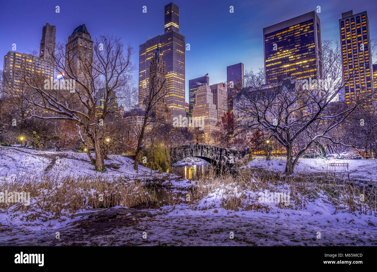 Winter Szene von Gapstow Brücke im Central Park in New York mit beleuchteten Hochhaus im Hintergrund. Umgebung und Bäumen bedeckt mit weißem Schnee. Stockfoto