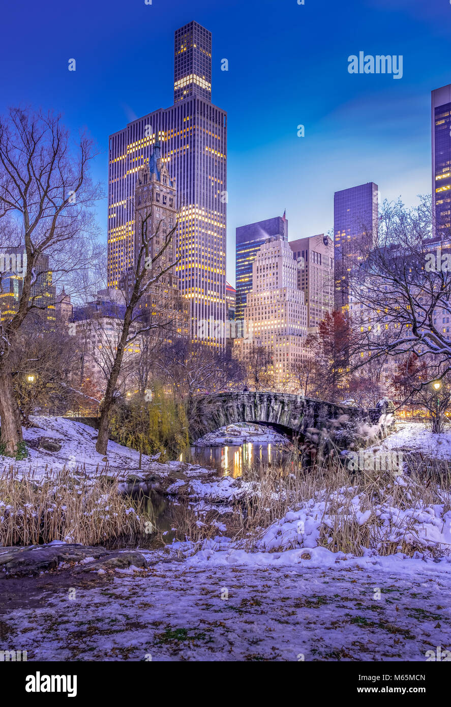 Winter Szene von Gapstow Brücke im Central Park in New York mit beleuchteten Hochhaus im Hintergrund. Umgebung und Bäumen bedeckt mit weißem Schnee. Stockfoto