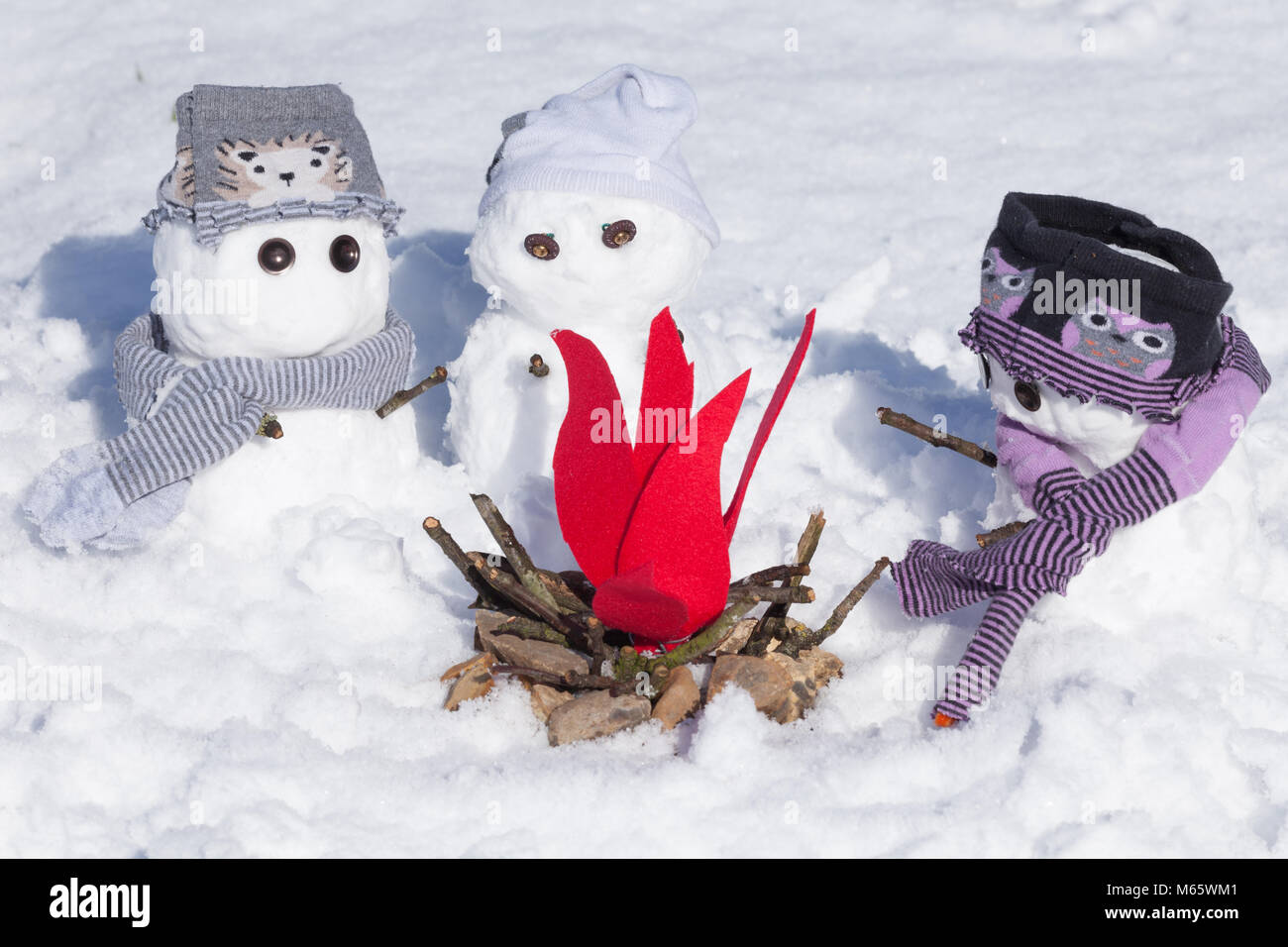Süße kleine Schneemänner gekleidet für den Winter, drängten sich um ein Feuer, die versuchen, warm zu halten. Verschneite Szene in Norfolk UK Stockfoto
