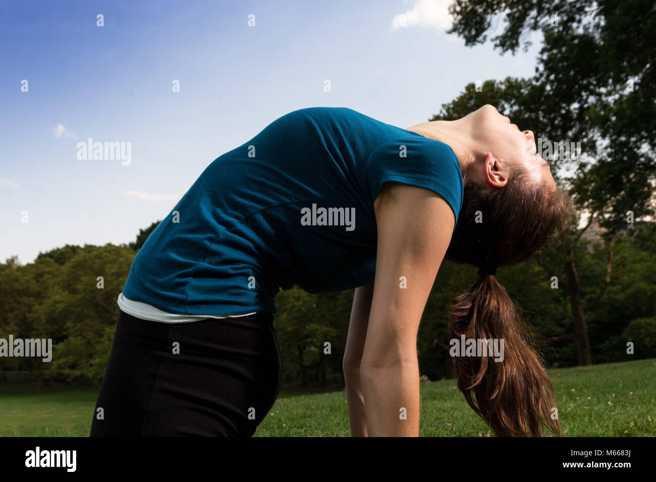 Junge kaukasier Frau übt Yoga im Central Park in New York City während trägt ein blaues Top, schwarze Leggings und barfuss Stockfoto