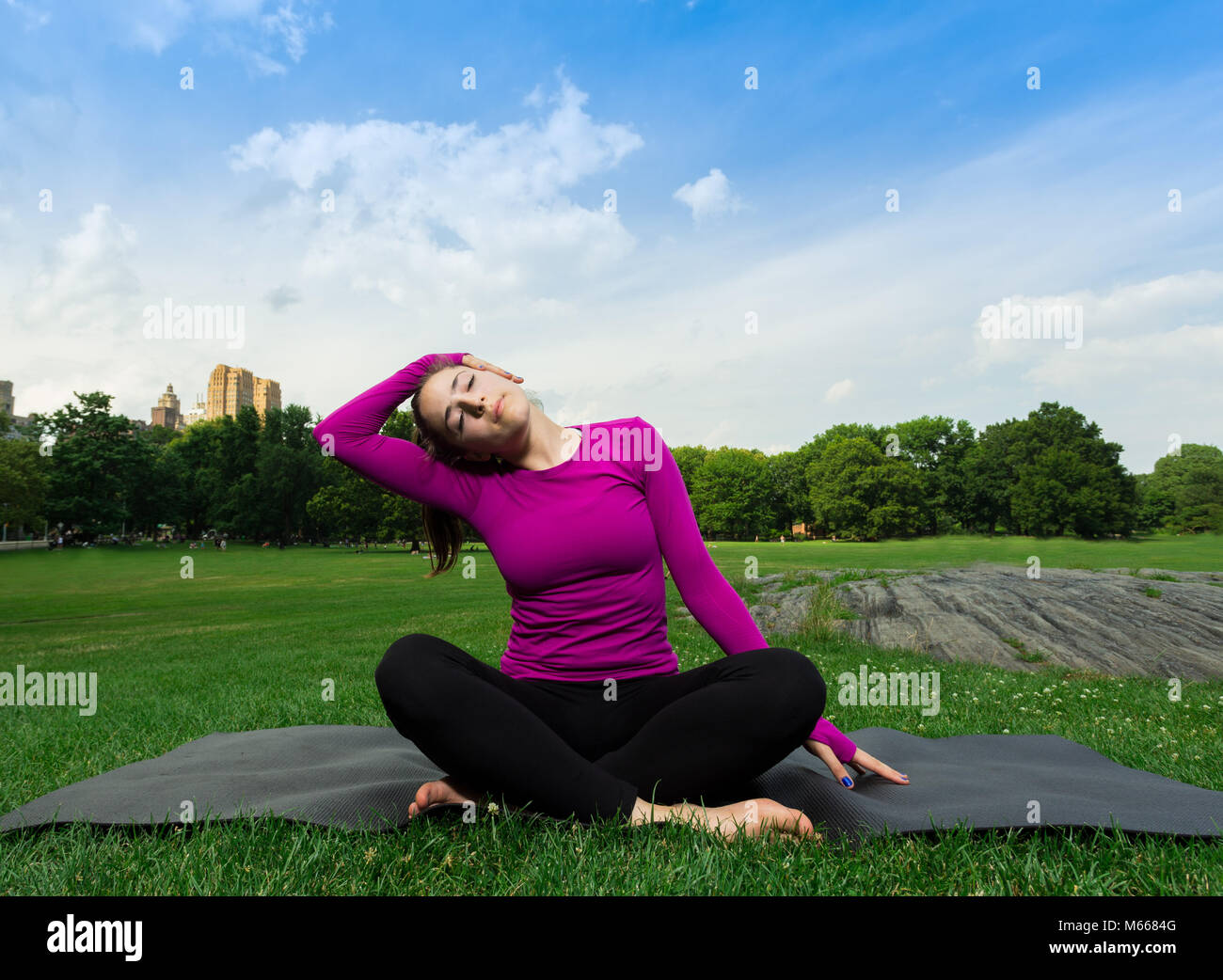 Junge kaukasier Frau übt Yoga im Central Park in New York City beim Tragen eines Magenta Top, schwarze Leggings und barfuss Stockfoto