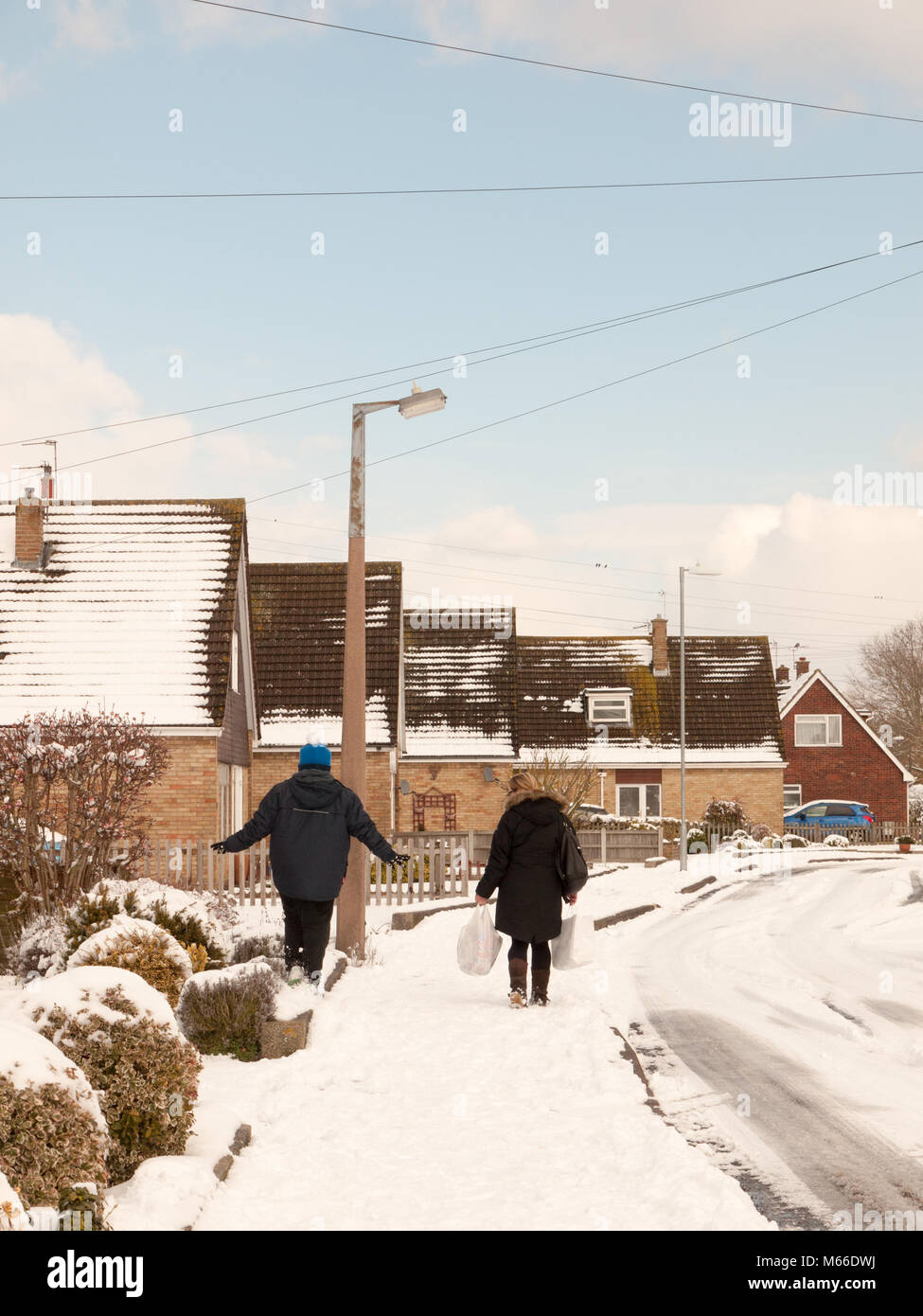 Mutter und Sohn gehen hinunter die Straße mit Schnee im Winter uk Estate von hinten, Essex, England, Großbritannien Stockfoto