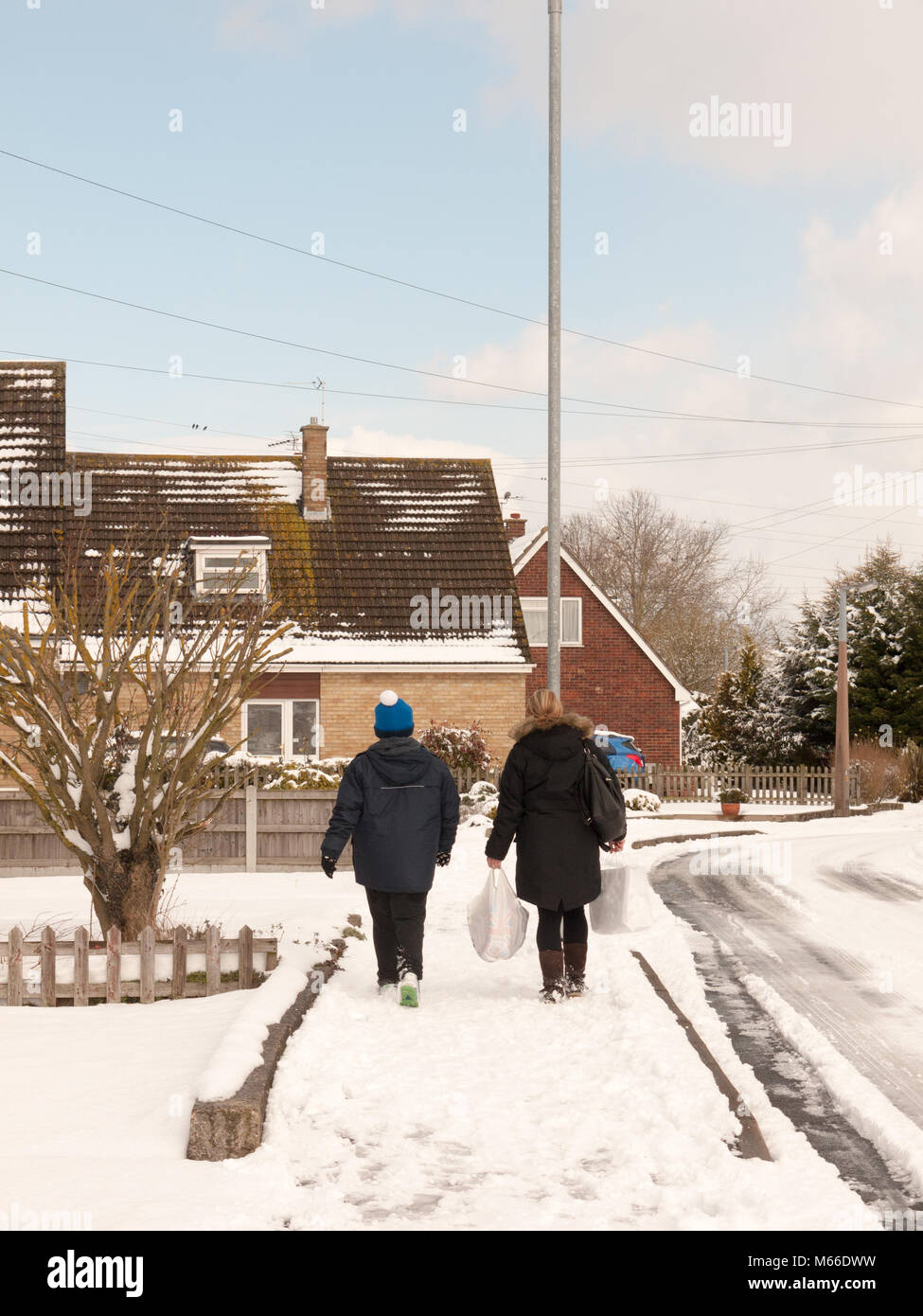 Mutter und Sohn gehen hinunter die Straße mit Schnee im Winter uk Estate von hinten, Essex, England, Großbritannien Stockfoto