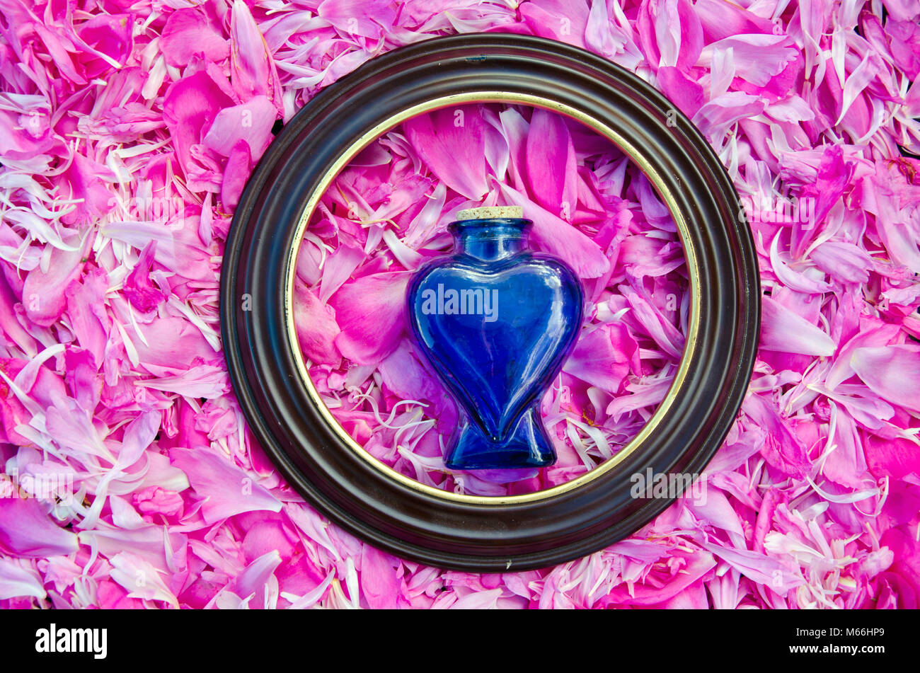 Runden Rahmen und vintage Parfum Duft blaues Herz form Flasche auf frische Pfingstrose Blütenblätter Hintergrund Stockfoto