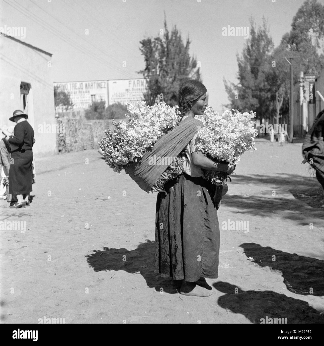 1930er Jahre Frau das TRAGEN UND DEN VERKAUF VON GROSSEN BÜNDEL VON BLUMEN IM DORF VON XOCHIMILCO MEXIKO-r 10284 HAR 001 HARS LANDWIRTSCHAFT 20-25 JAHRE NORDAMERIKA MEXIKO VERKAUF STÄRKE LAST 18-19 JAHRE BARFUSS WACHSTUM EINE PERSON MIT ANDEREN NATIVE AMERICAN INDIANER JUNGE ERWACHSENE FRAU B&W schwarze und weiße Blüten BUNDLES KEINE SCHUHE BERUFE ALTMODISCHE PERSONEN XOCHIMILCO Stockfoto