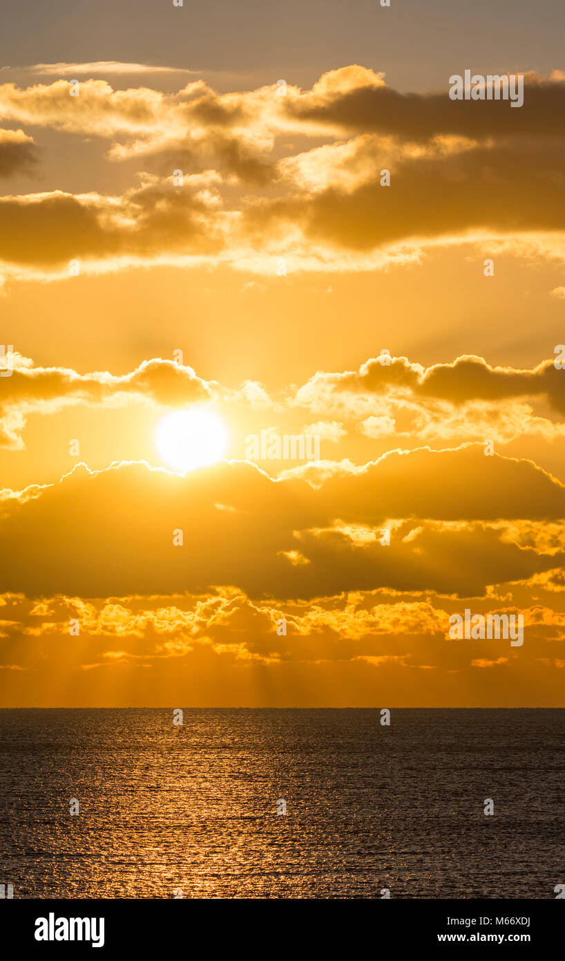 Sonnenuntergang über dem Meer mit uneinheitlichen Wolken und Sonne, die Spiegelungen im Wasser im Winter, UK. Stockfoto