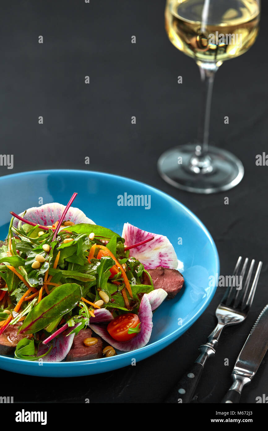 Würziges Rindfleisch Scheiben Fleisch Salat mit Tomaten, Petersilie, Radieschen und Salat Spinat auf schwarze Textur Hintergrund Tabelle Stockfoto