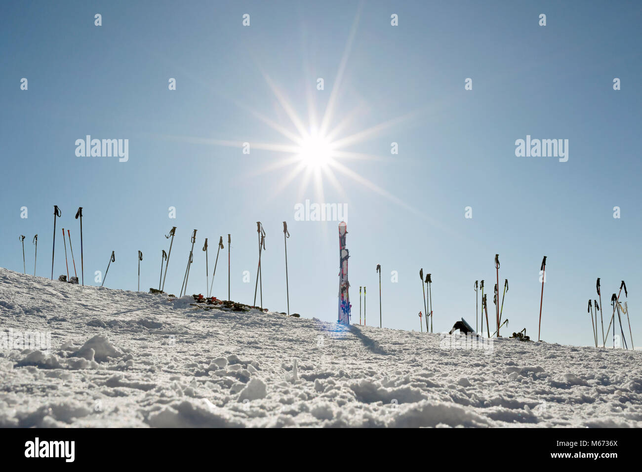 Skier und Stöcke gepflanzt, die in den Schnee an der Seite der Piste in Österreich mit einem hellen Sonne int der Himmel Stockfoto