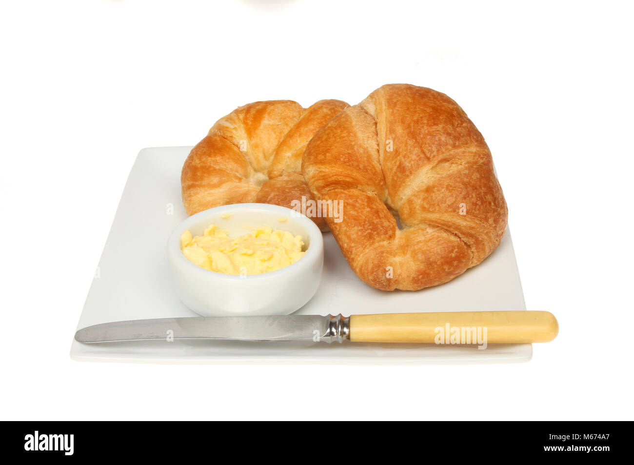 Croissants Butter und ein Messer auf einer Platte gegen Weiße isoliert Stockfoto