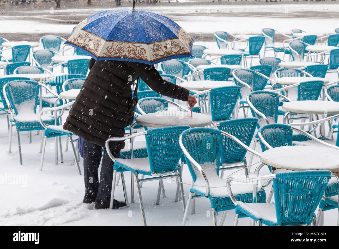 Venedig, Venetien, Italien, 1. März 2018. Schlechtes Wetter in Venedig heute mit Sub-Temperaturen zwischen minus 3 und minus 2 und kontinuierliche Schnee den ganzen Tag durch das Tier aus dem Osten, oder die Sibirische Front aus Russland quer durch Europa. die Frau unter einem Sonnenschirm Schreiben habe ich den Schnee auf einem Tisch im Restaurant auf der Piazza San Marco. Stockfoto