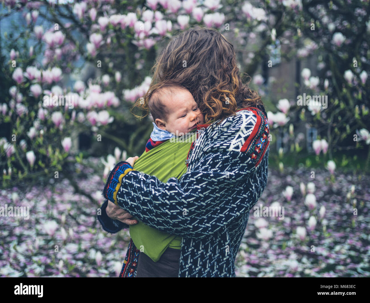 Eine junge Mutter mit ihrem schreienden Baby im Tragetuch steht der Magnolie Stockfoto